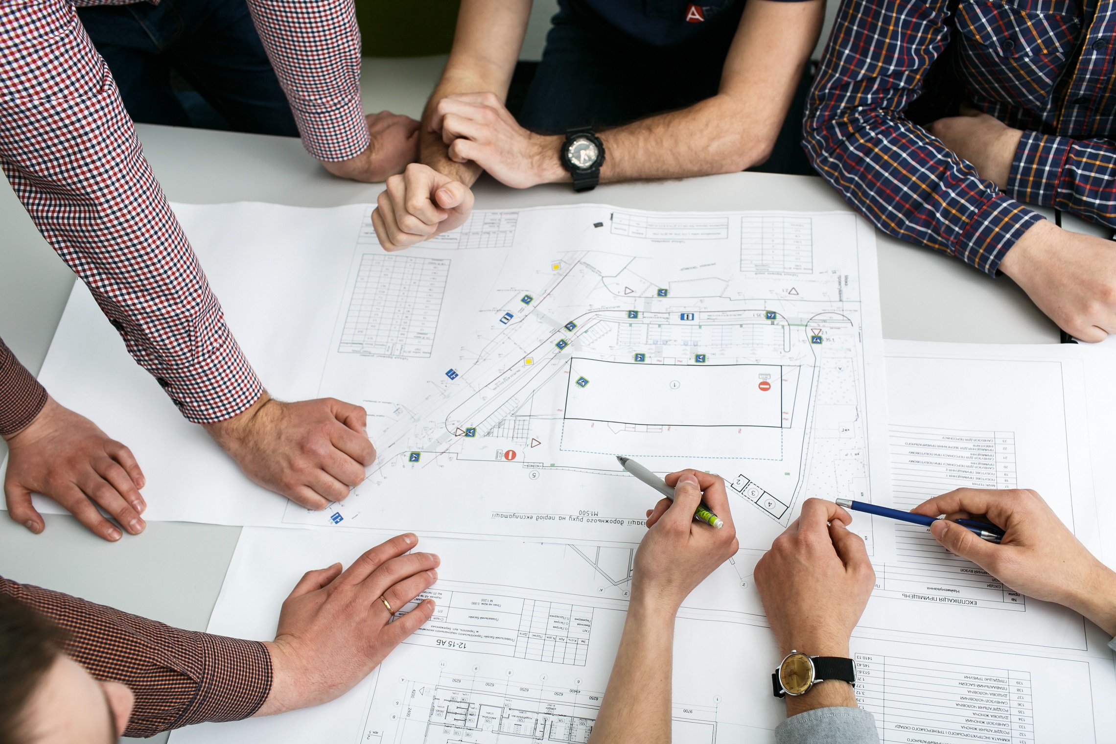 table-with-blueprints-hands-holding-pencils